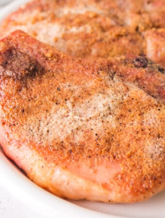 Close-up of juicy smoked pork chops with a crispy rub, served on a white plate with parsley garnish