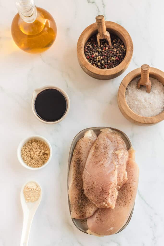 Overhead view of raw chicken breasts with marinade ingredients on marble surface