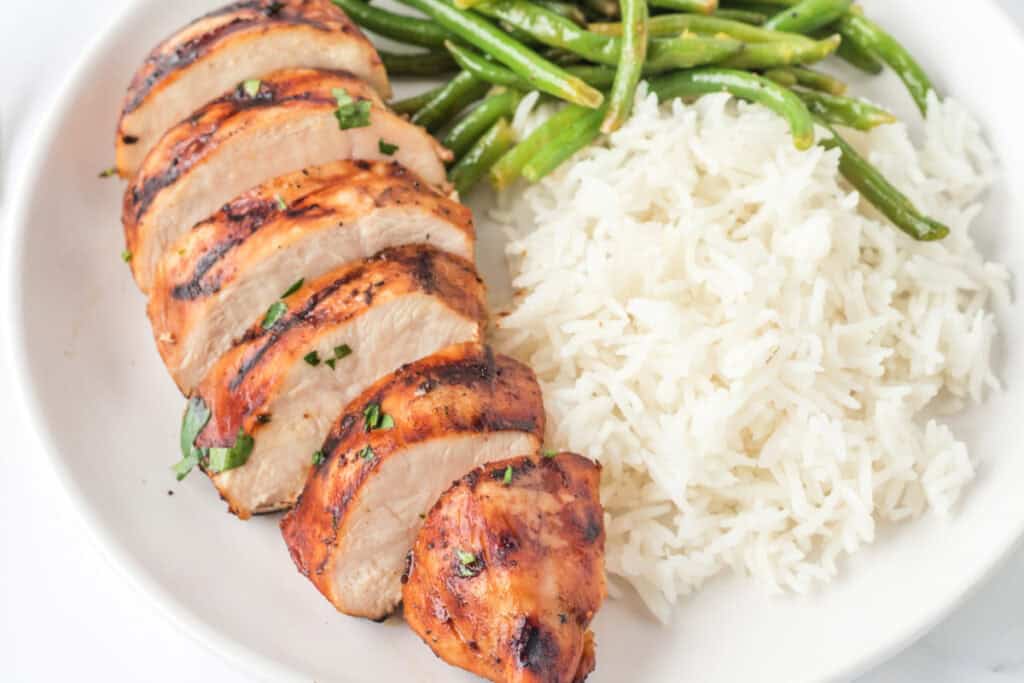 Sliced balsamic grilled chicken breast served on a plate with rice and green beans