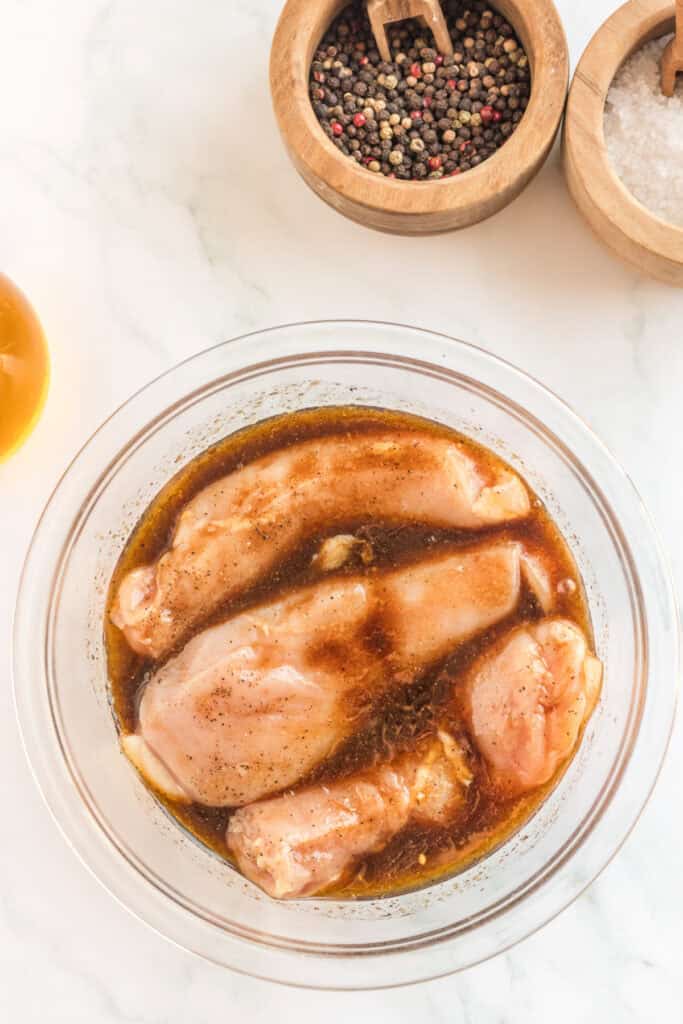 Chicken breasts soaking in balsamic marinade in a glass bowl