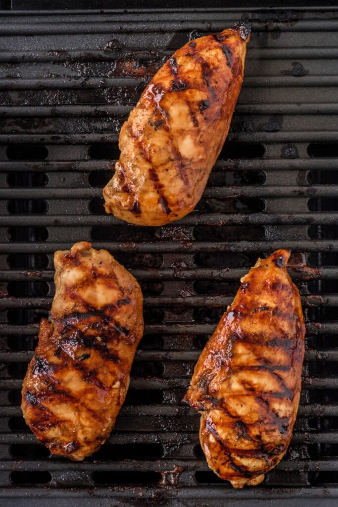 Three balsamic-marinated chicken breasts grilling with char marks