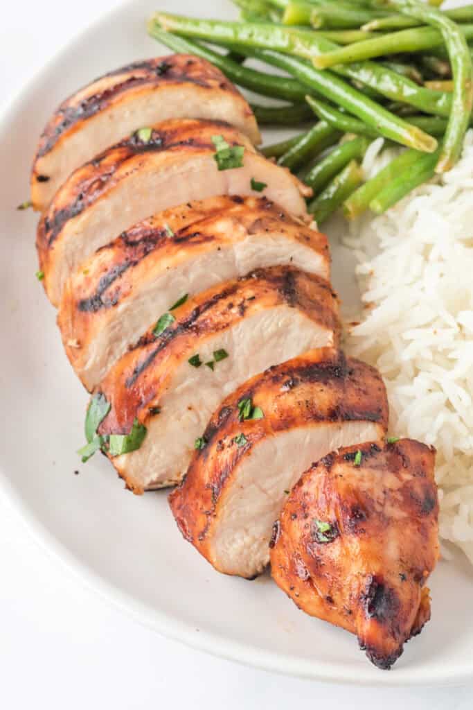 Angled shot of sliced grilled chicken breast with visible char and fresh herbs