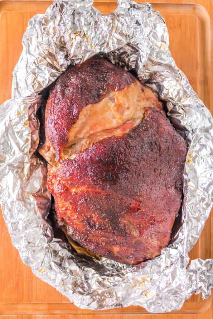 Finished Boston butt resting in foil on a wooden cutting board.