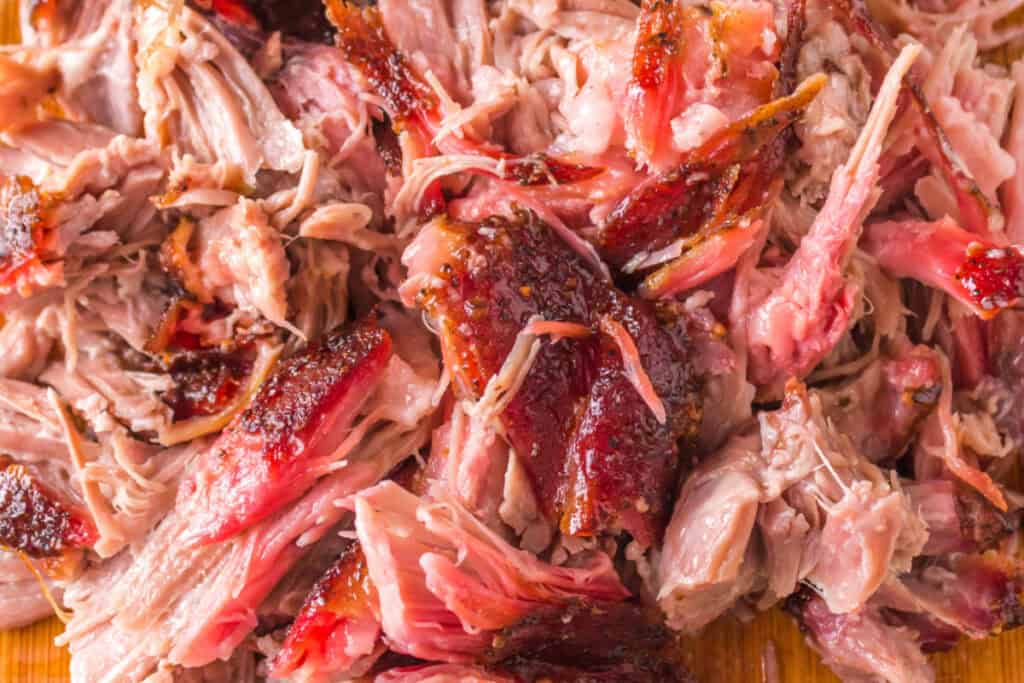 Close-up of shredded grilled pulled pork showing bark and juicy interior.