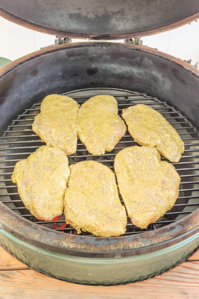 Marinated chicken breasts placed on a hot grill inside a smoker