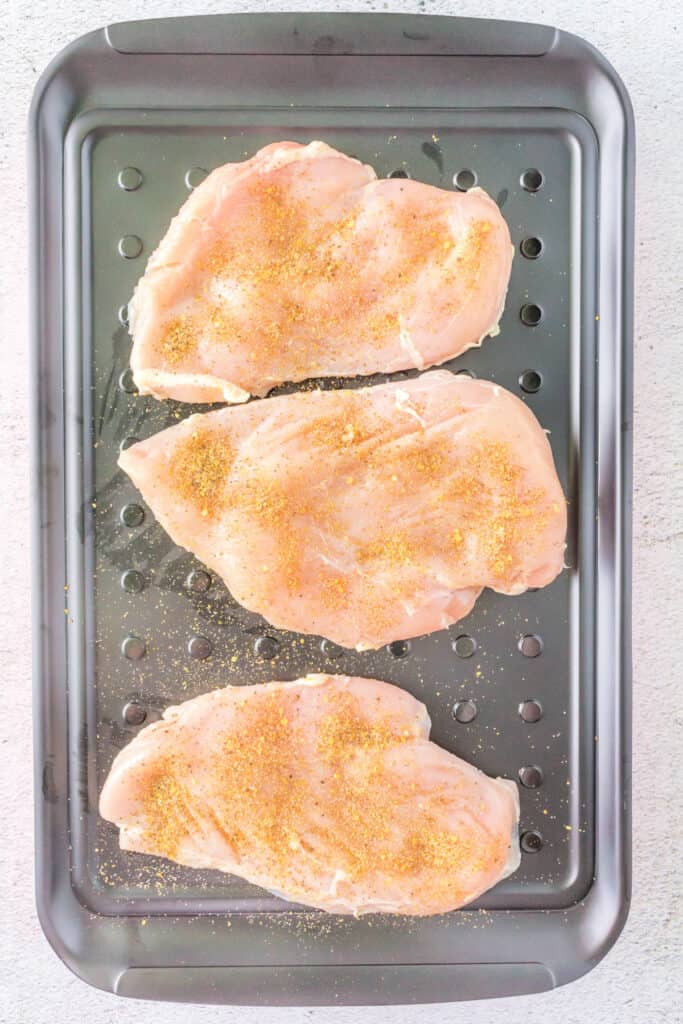 Chicken breasts coated with a dry spice rub on a marinade tray
