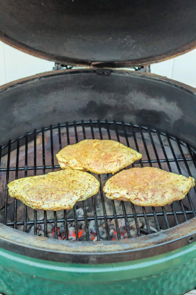 Seasoned raw chicken breasts placed on the grill grates inside a Big Green Egg.