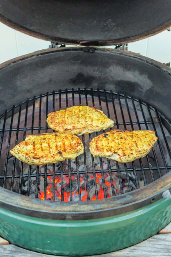 Lemon pepper chicken breasts cooking on a hot grill with visible sear marks.