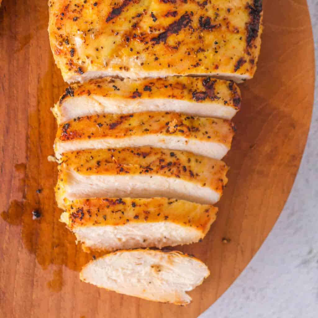 Overhead view of sliced grilled lemon pepper chicken breast on a wooden board.