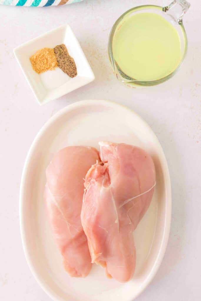 Raw chicken breasts on a white plate with spices and Margarita mix nearby