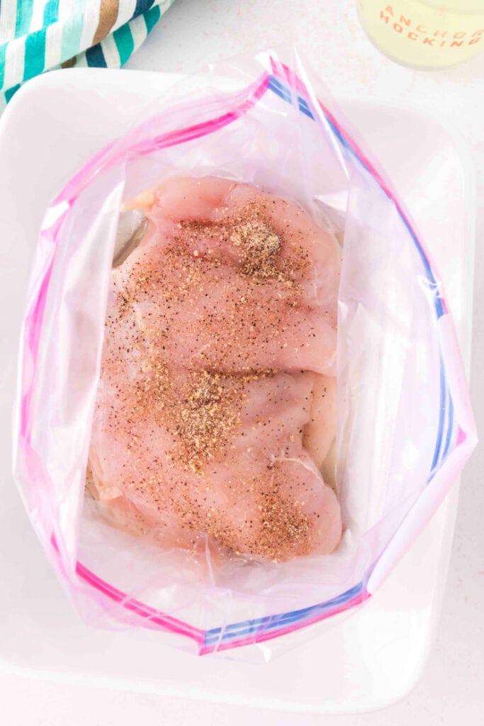 Seasoned chicken breasts in a zip-top bag ready for marinating