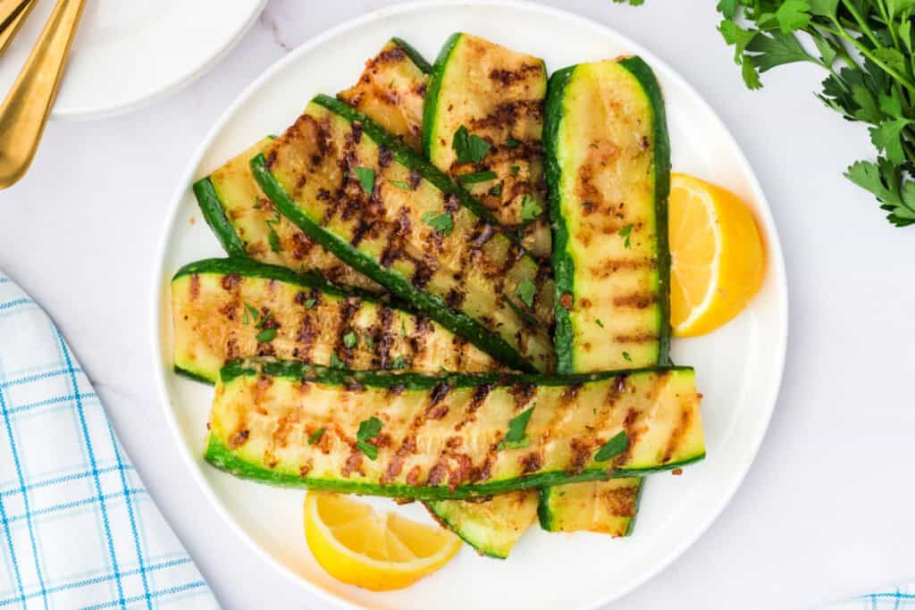 Top view of a plate filled with grilled zucchini strips and fresh parsley, served with lemon.