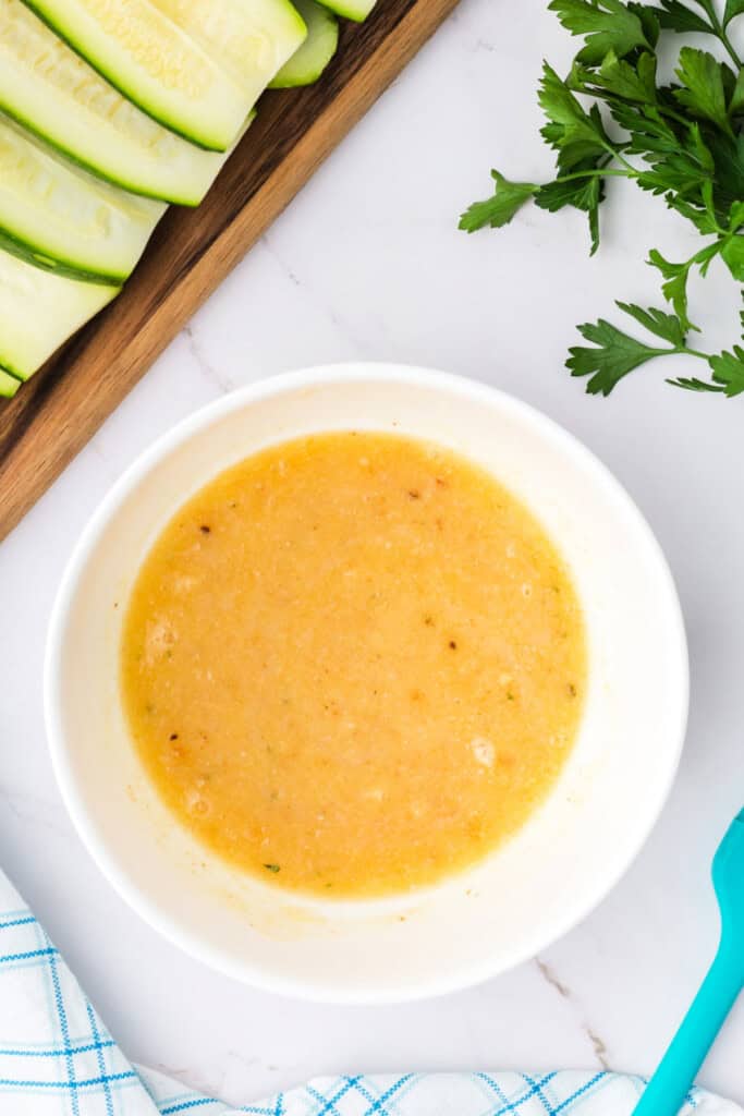 Butter mixture fully combined in a white bowl next to zucchini strips.