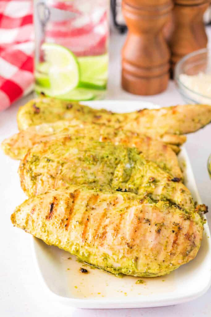 Grilled pesto chicken breasts served on a white plate, garnished and ready to eat.