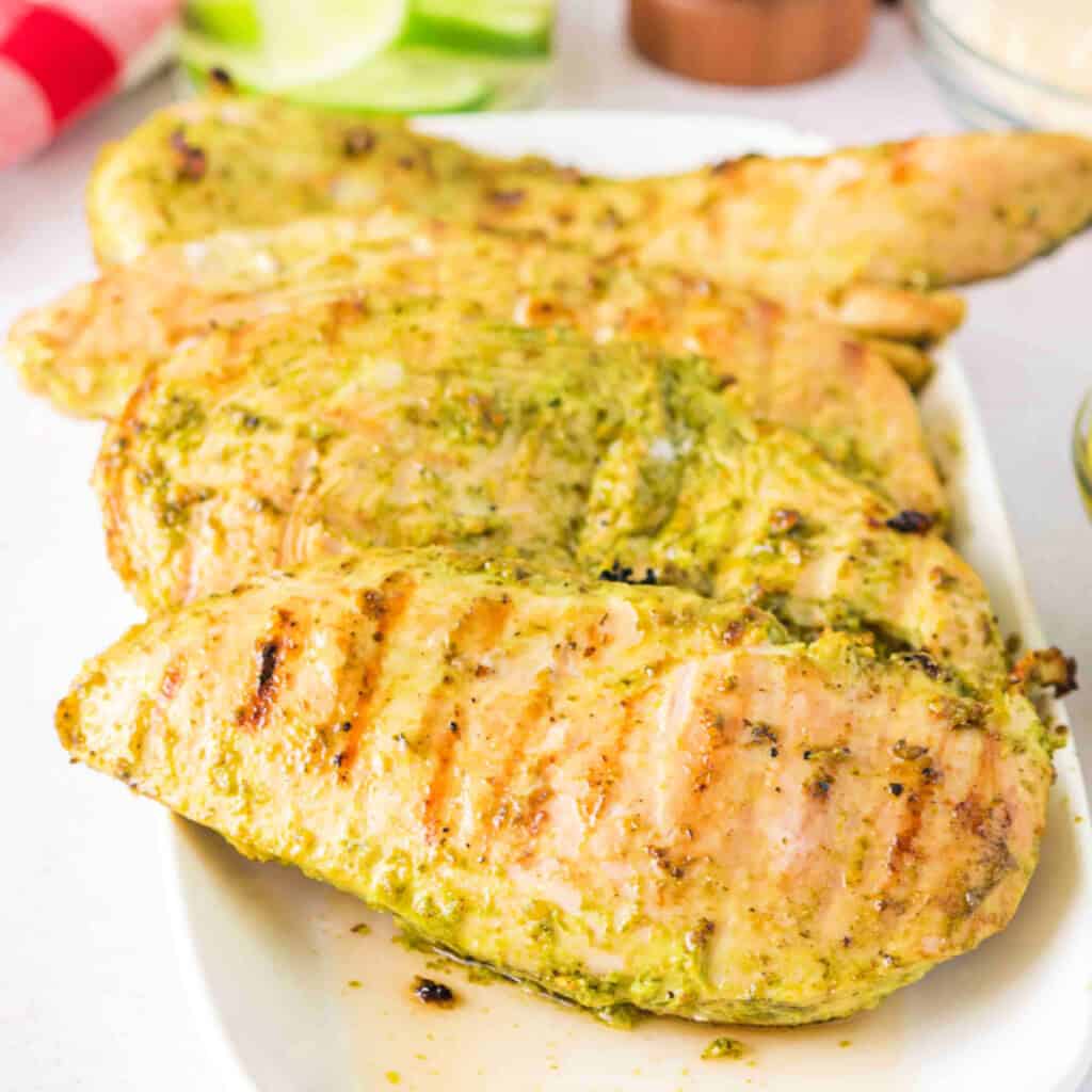 Close-up of grilled pesto chicken stacked on a serving plate.