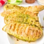 Close-up of grilled pesto chicken stacked on a serving plate.