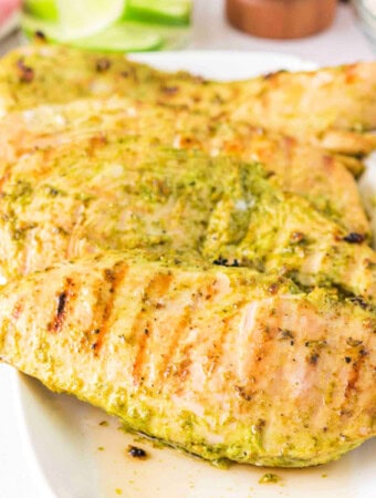 Close-up of grilled pesto chicken stacked on a serving plate.