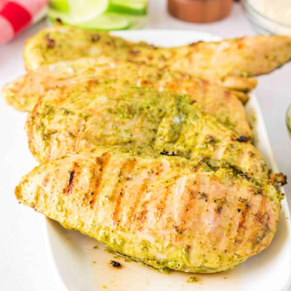 Close-up of grilled pesto chicken stacked on a serving plate.