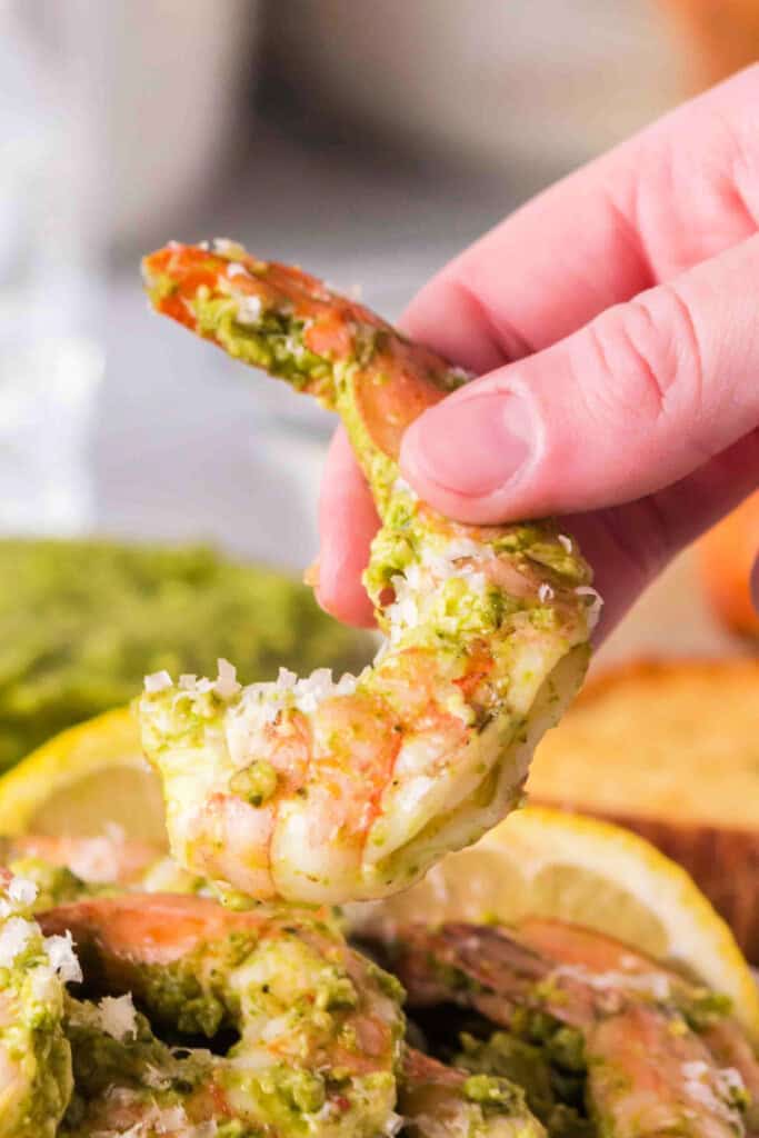 Hand holding a single grilled pesto shrimp, topped with cheese