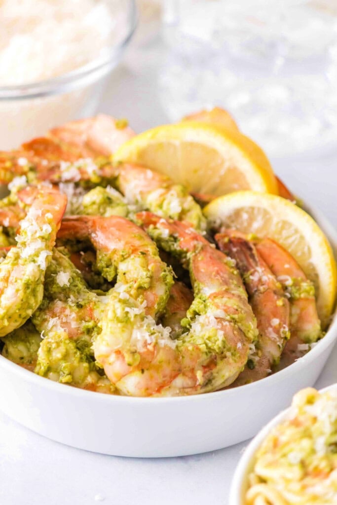 Bowl of grilled pesto shrimp garnished with lemon slices and cheese