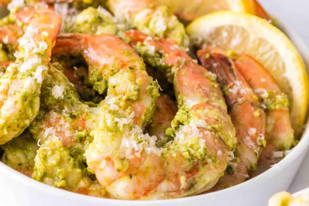 Close-up of grilled pesto shrimp in a bowl with grated cheese and lemons