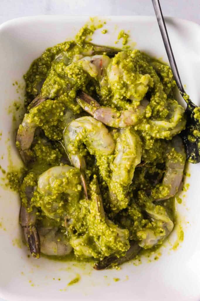 Shrimp coated in bright green basil pesto marinade in a bowl with a spoon