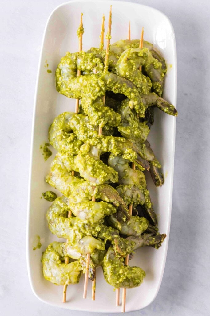 Shrimp skewered and coated in pesto, arranged on a white platter