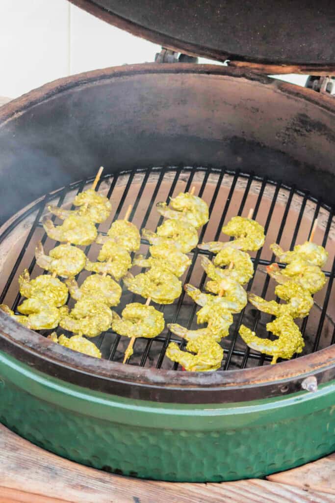 	Shrimp skewers placed on a smoky grill, beginning to cook
