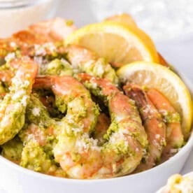 Overhead view of grilled pesto shrimp in a bowl, garnished with lemons