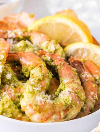 Overhead view of grilled pesto shrimp in a bowl, garnished with lemons