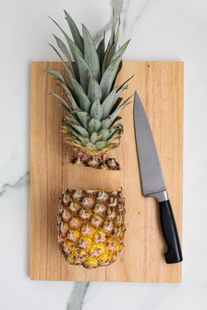 Pineapple with top removed on a cutting board next to a chef’s knife