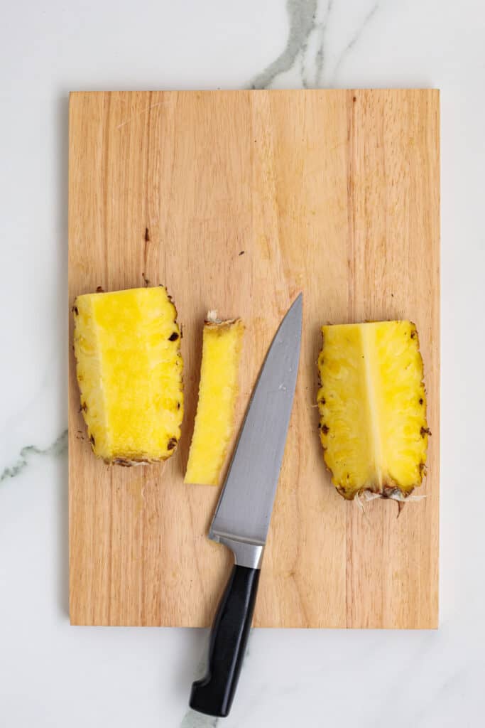 Knife removing the core from pineapple halves on cutting board