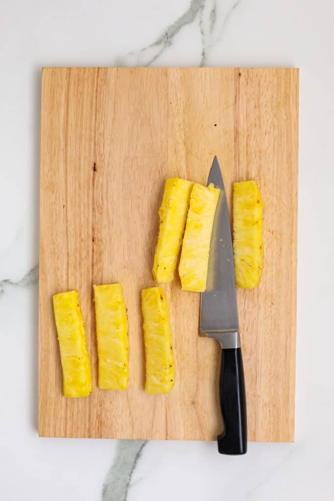 Pineapple sliced into spears on a wooden cutting board