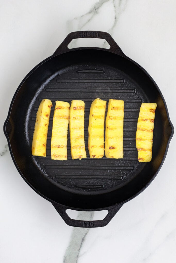 Pineapple spears arranged on a cast iron grill pan with visible grill marks