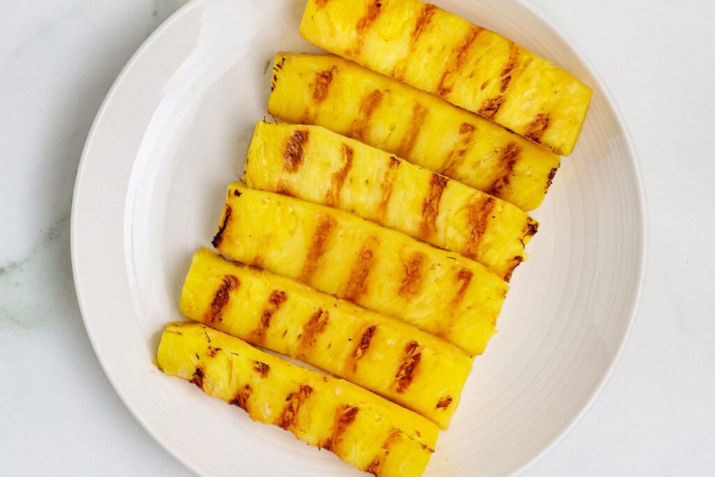 Landscape view of grilled pineapple spears with caramelized grill marks on a white plate