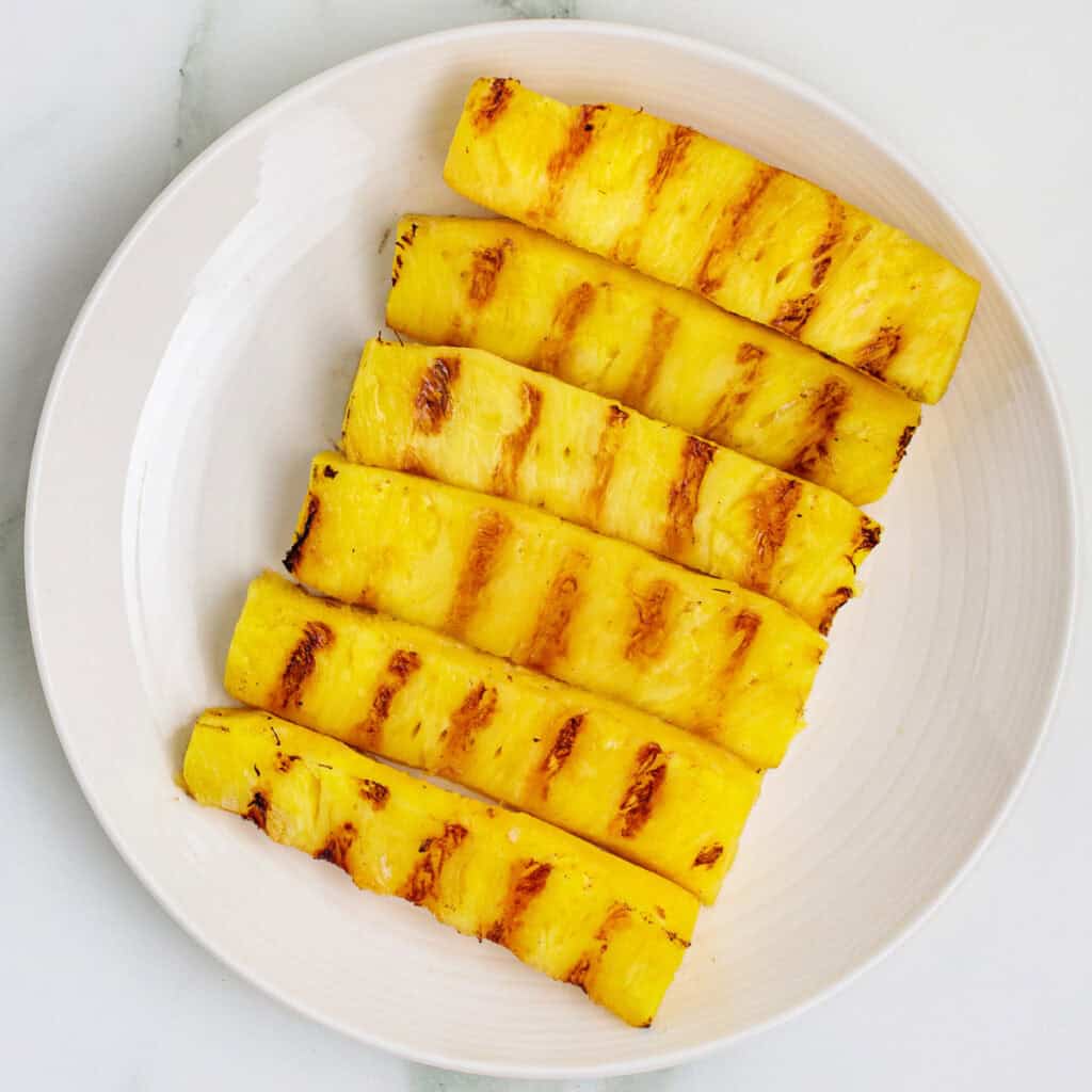 Square crop of grilled pineapple spears with charred grill marks on a white plate
