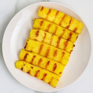 Square crop of grilled pineapple spears with charred grill marks on a white plate