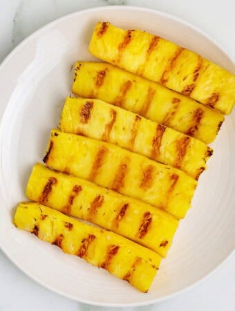 Square crop of grilled pineapple spears with charred grill marks on a white plate