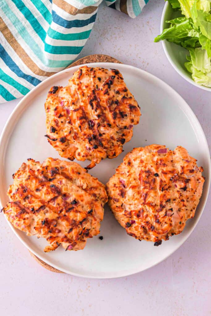 Grilled salmon burger patties resting on a plate with char marks visible