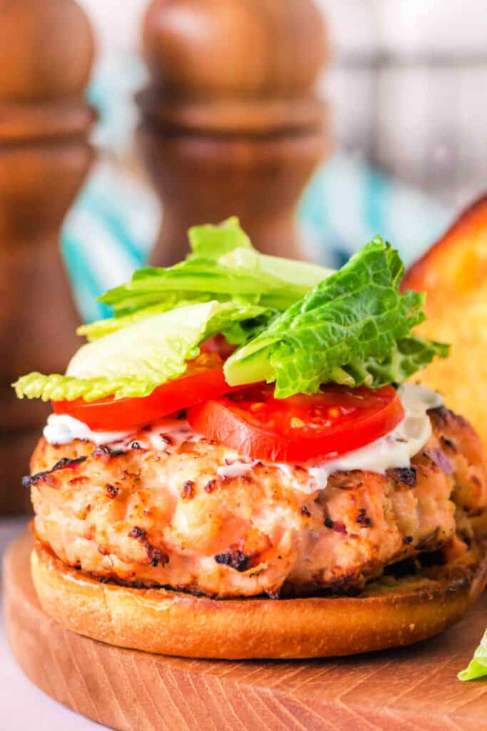 Close-up of a fully assembled grilled salmon burger with lettuce and tomato