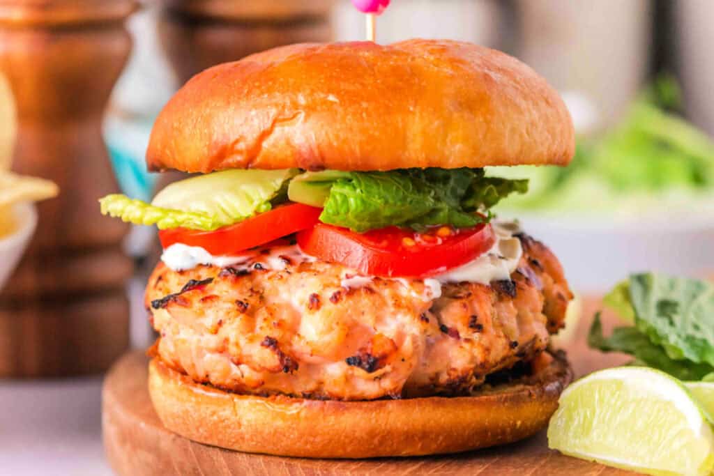 Salmon burger on brioche bun with lettuce, tomato, and mayonnaise, lime wedge on the side