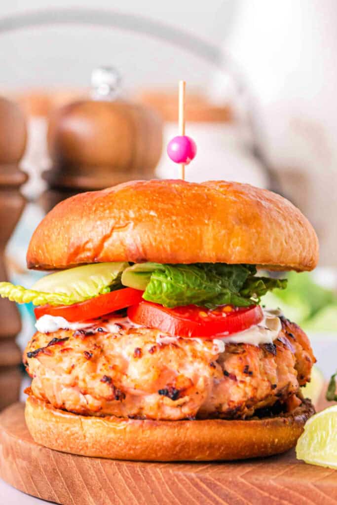 Side view of a grilled salmon burger stacked with toppings on a wooden board