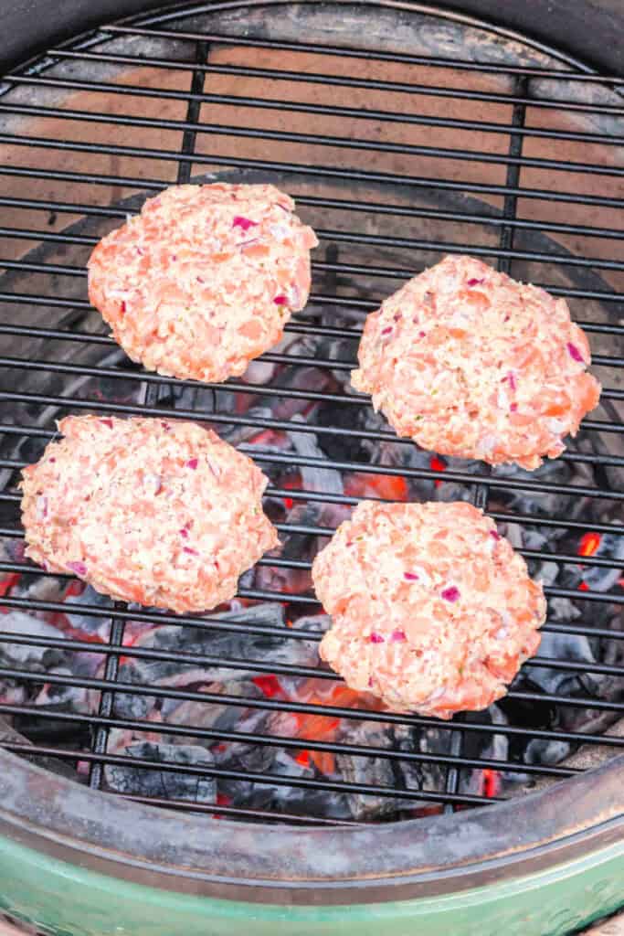 Raw salmon burger patties placed on a hot grill with visible coals