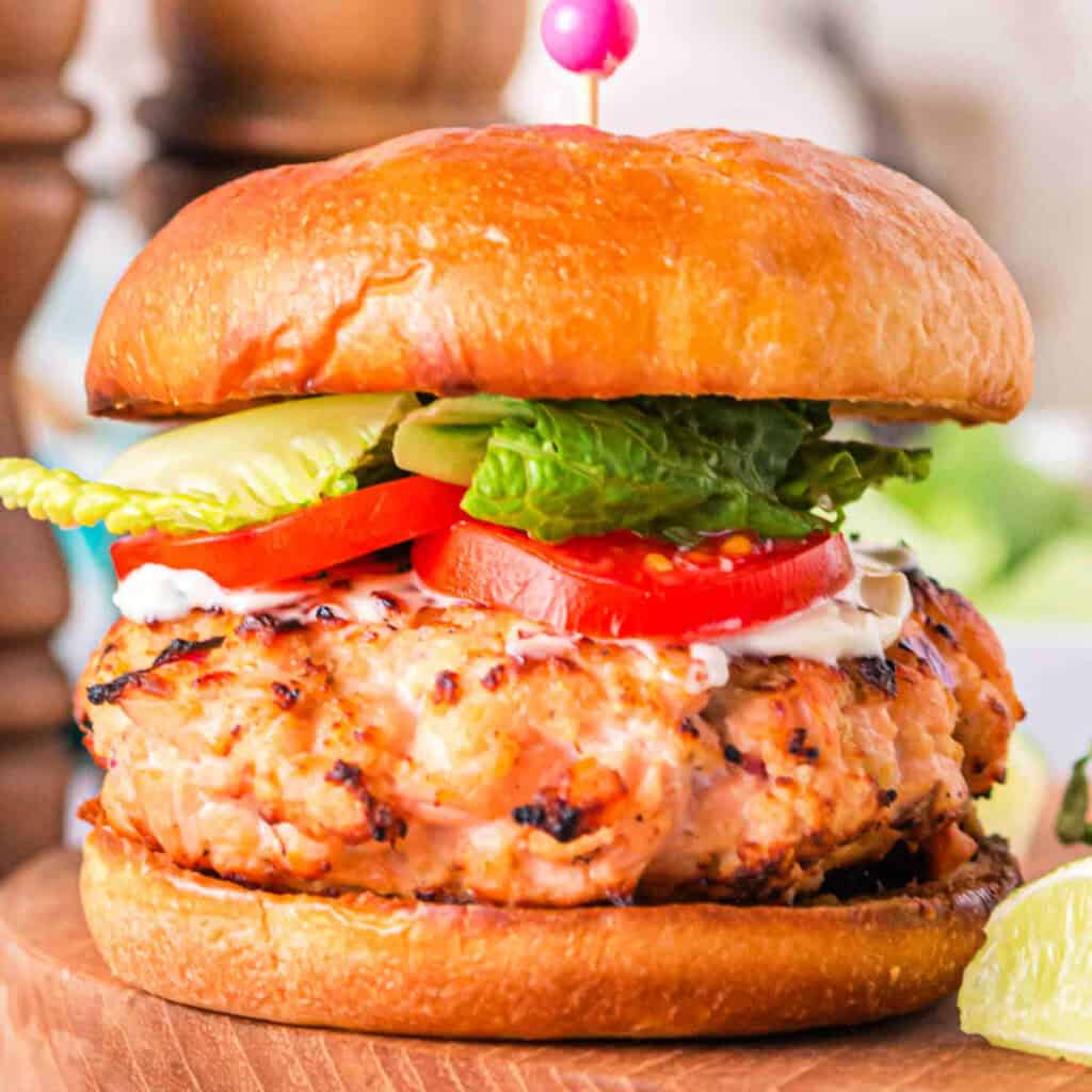 Square close-up of a grilled salmon burger on a brioche bun with lettuce, tomato, and mayo