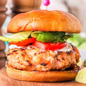 Square close-up of a grilled salmon burger on a brioche bun with lettuce, tomato, and mayo