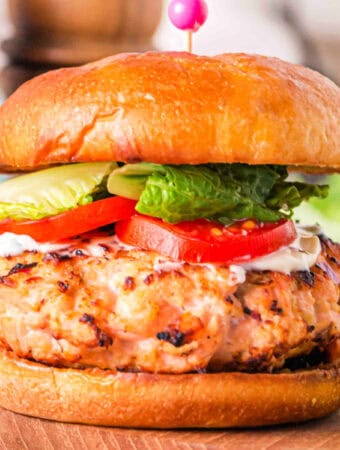 Square close-up of a grilled salmon burger on a brioche bun with lettuce, tomato, and mayo