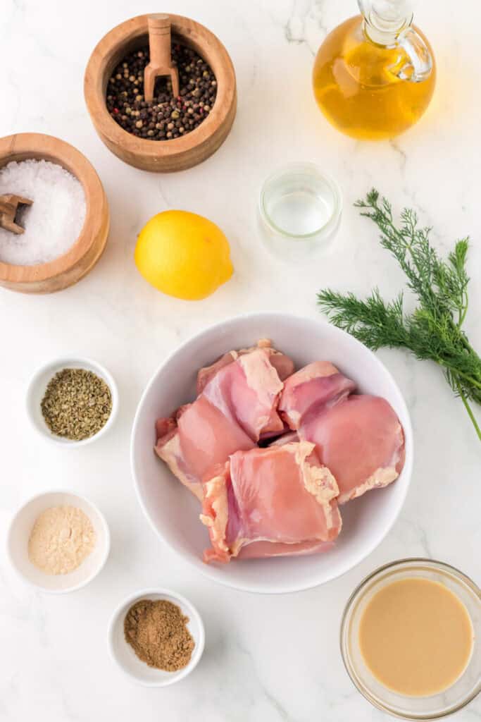 Overhead view of raw ingredients for tahini chicken including chicken thighs, lemon, tahini, oil, spices, and herbs.