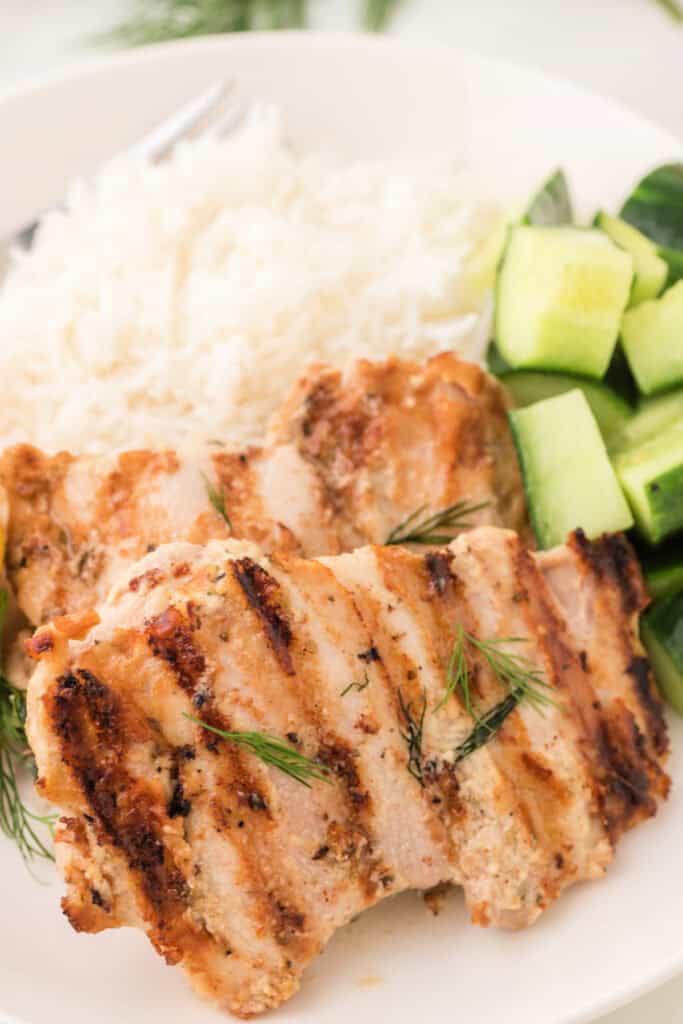 Grilled tahini chicken served with white rice and cucumber salad on a white plate.