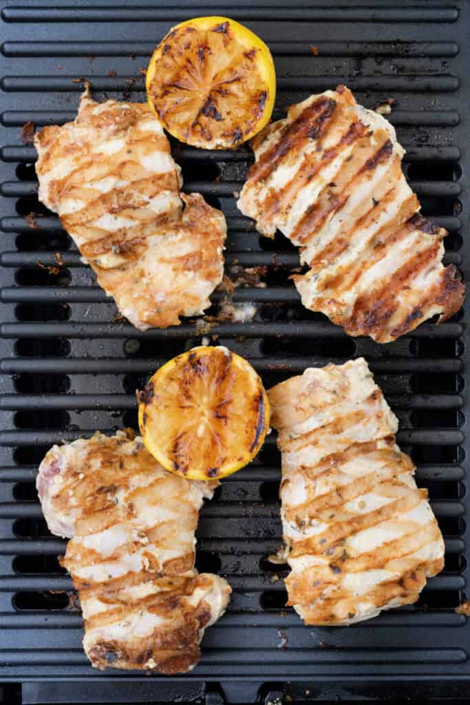 Grilled tahini chicken cooking on a grill pan with charred lemon halves.