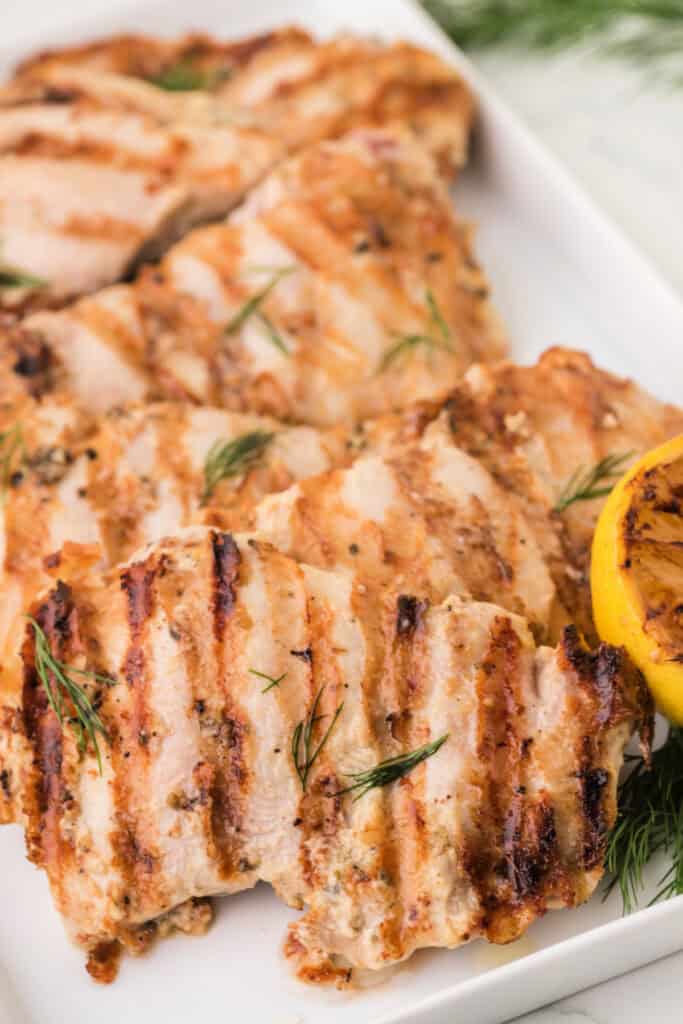 Close-up of grilled tahini chicken garnished with fresh dill on a serving platter.